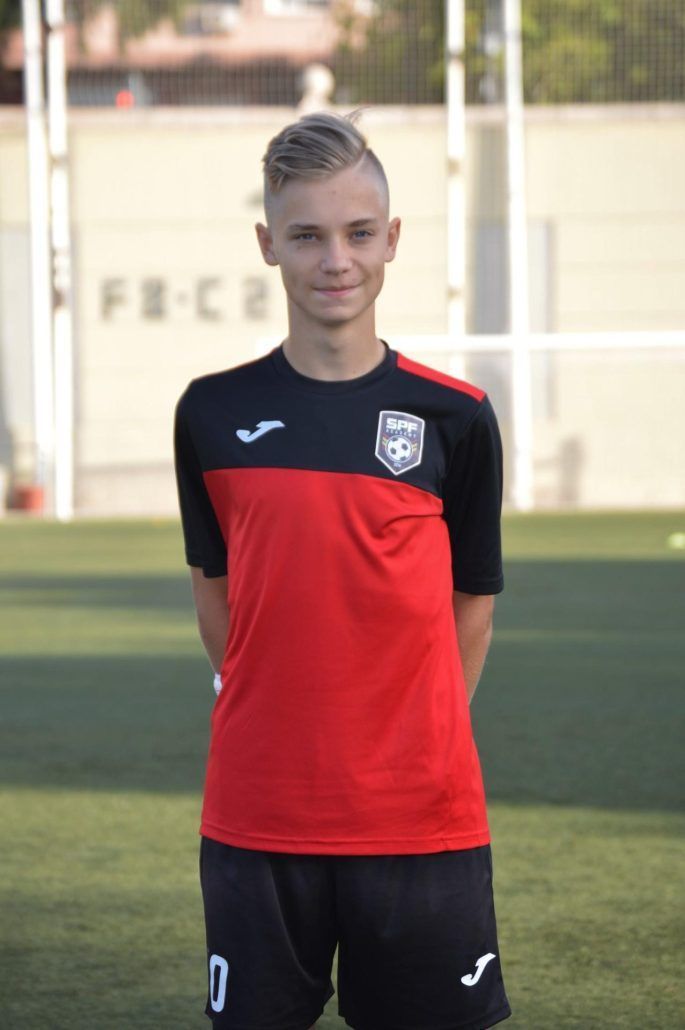 Soccer player in red-and-black uniform standing on a field, facing the camera.