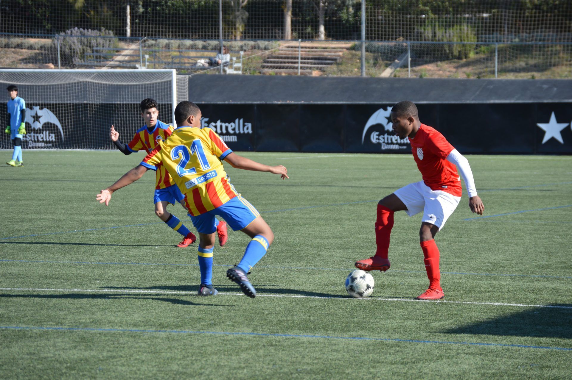 Soccer players in red and yellow-blue uniforms contest the ball on a turf field.
