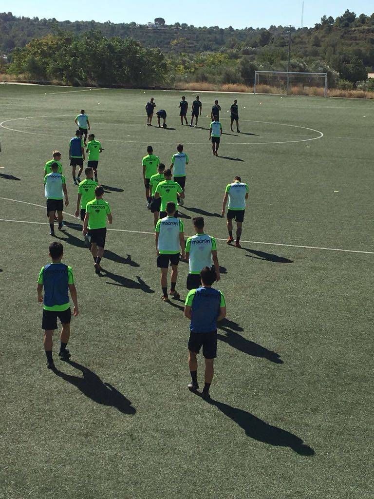 Soccer players in green and blue bibs practicing on a field in bright sunlight