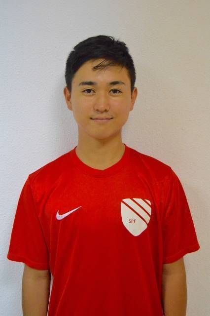 Person in a red sports jersey standing against a plain wall.