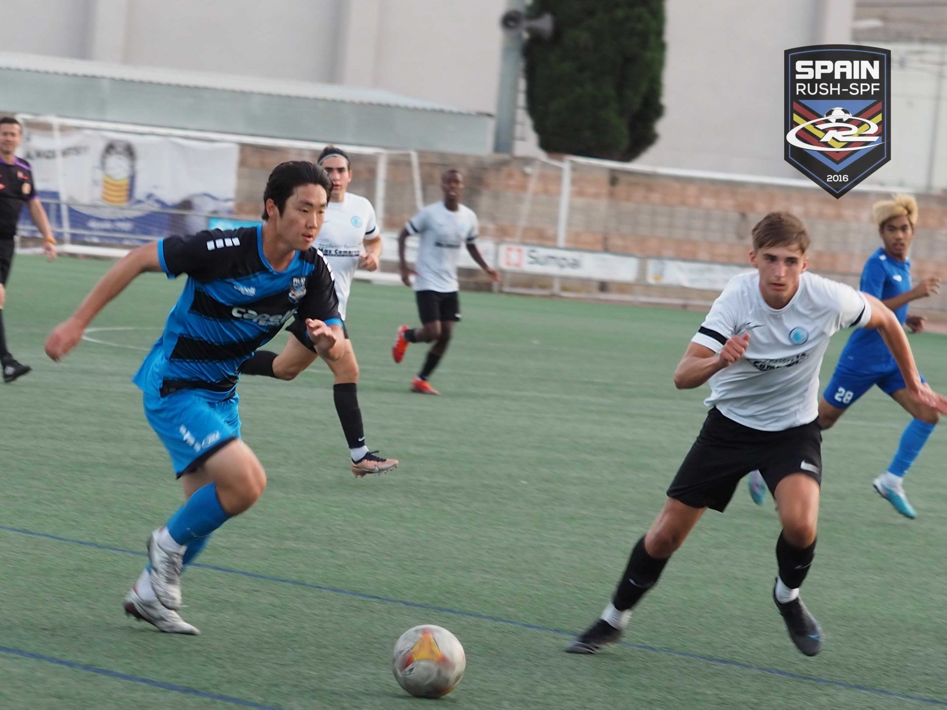 Soccer players in blue and white jerseys chase the ball on an outdoor field