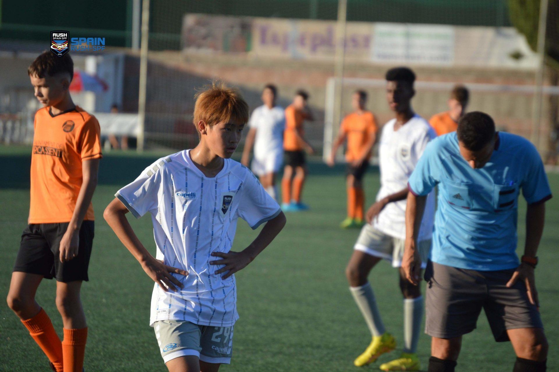 Soccer players standing on a field, with one in a white striped jersey and others in orange and blue shirts