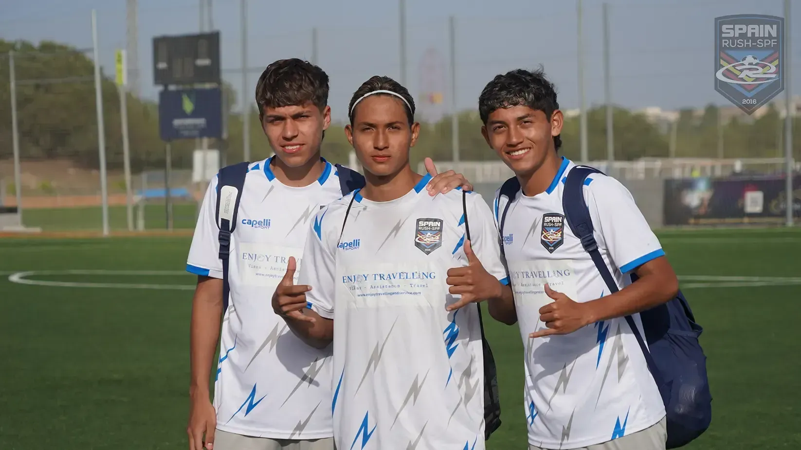 Three soccer players in white jerseys posing on a field, two giving thumbs up.