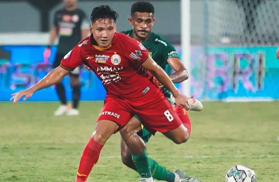 Two soccer players in red and green contest the ball during a match on the field.