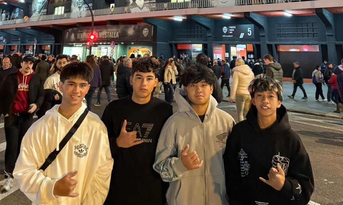 Four friends posing outside a busy venue at night, smiling and making hand gestures.