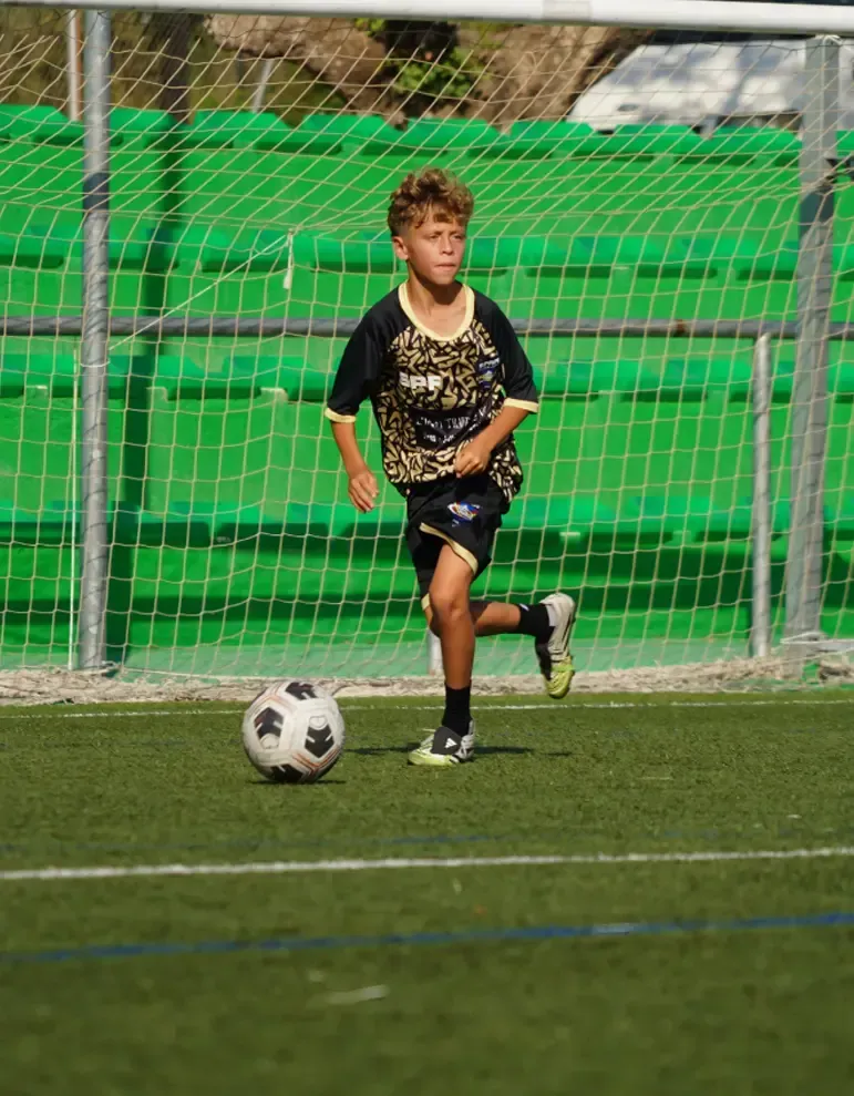 Young soccer player in black kit running near a goal with a soccer ball on the field
