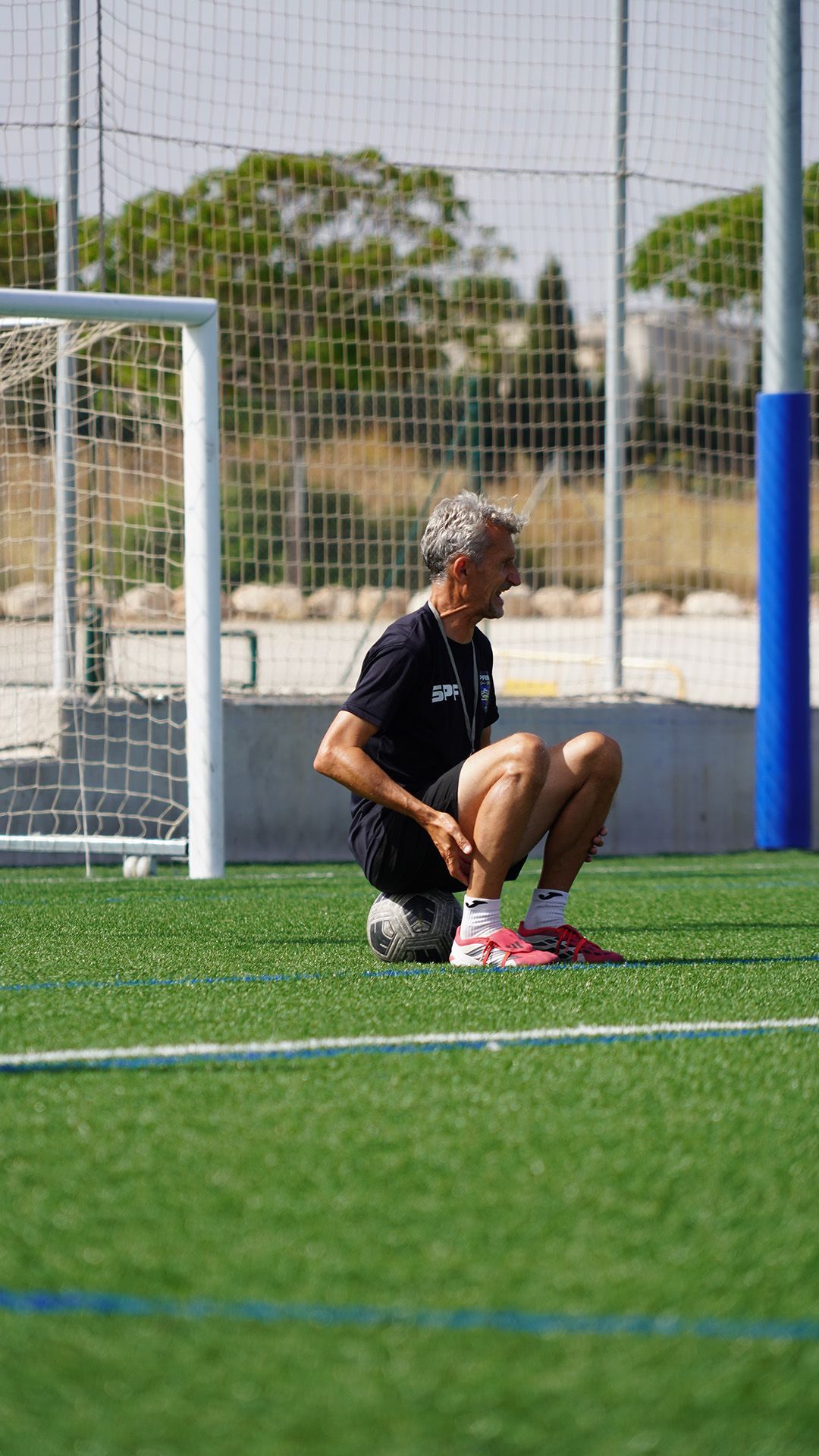 Soccer player kneeling on the field near a goal, wearing black and pink gear.