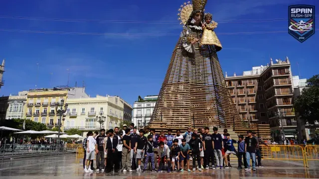 People posing in front of a giant woven sculpture in a sunny city square