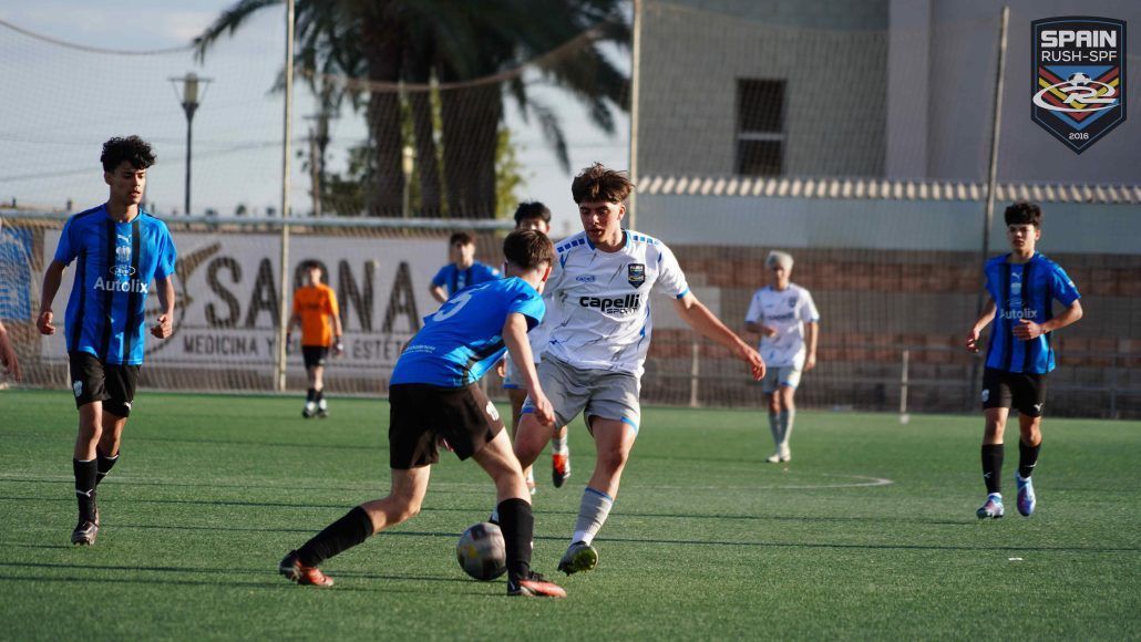 Soccer players in blue and white uniforms contest the ball on a sunny field