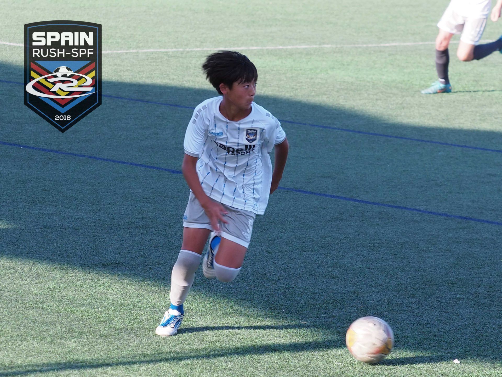 Soccer player in white dribbles a ball on a green field during a match