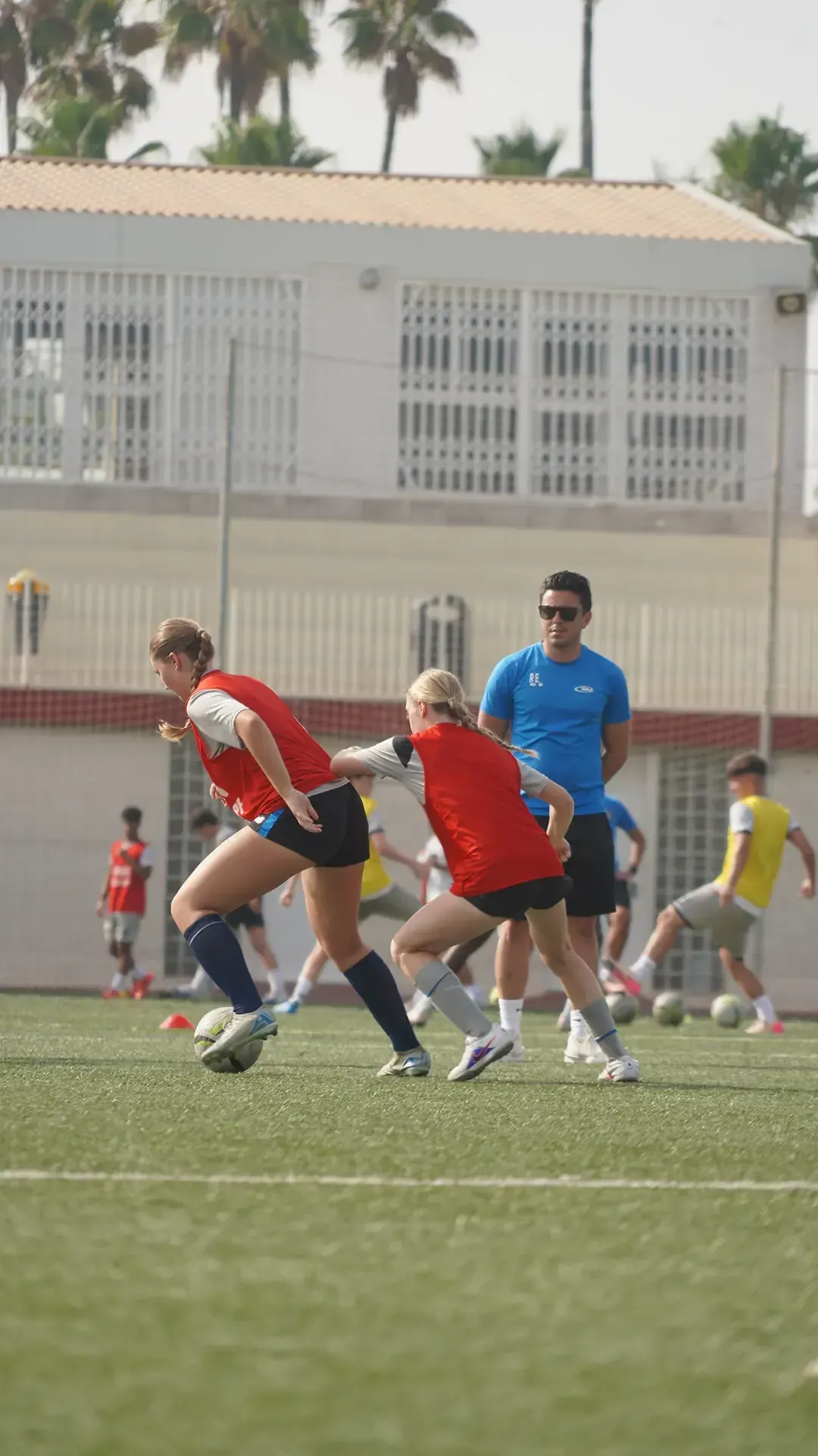 Soccer players in red and blue jerseys chase the ball on a grassy field.