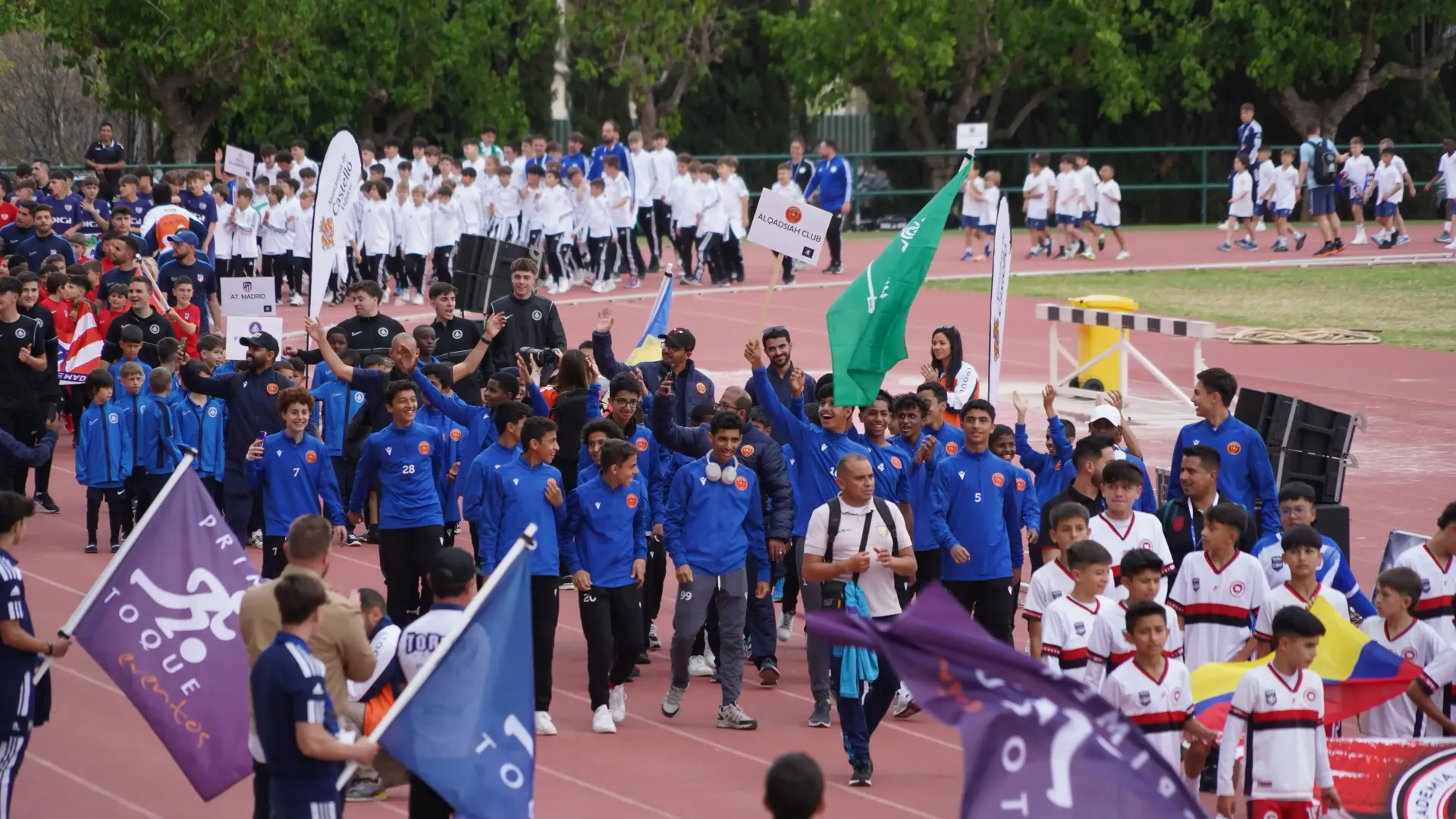 Students marching on a track during a school parade, carrying colorful flags and banners