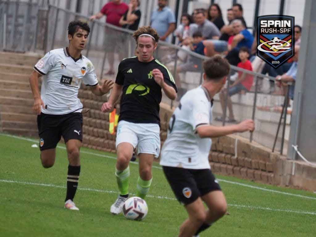 Soccer players in white and black jerseys contest the ball on a grassy field near the sideline.
