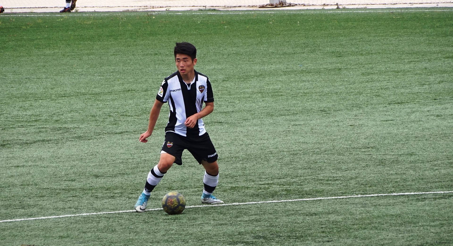 Soccer player in black-and-white kit dribbling a ball on a grassy field