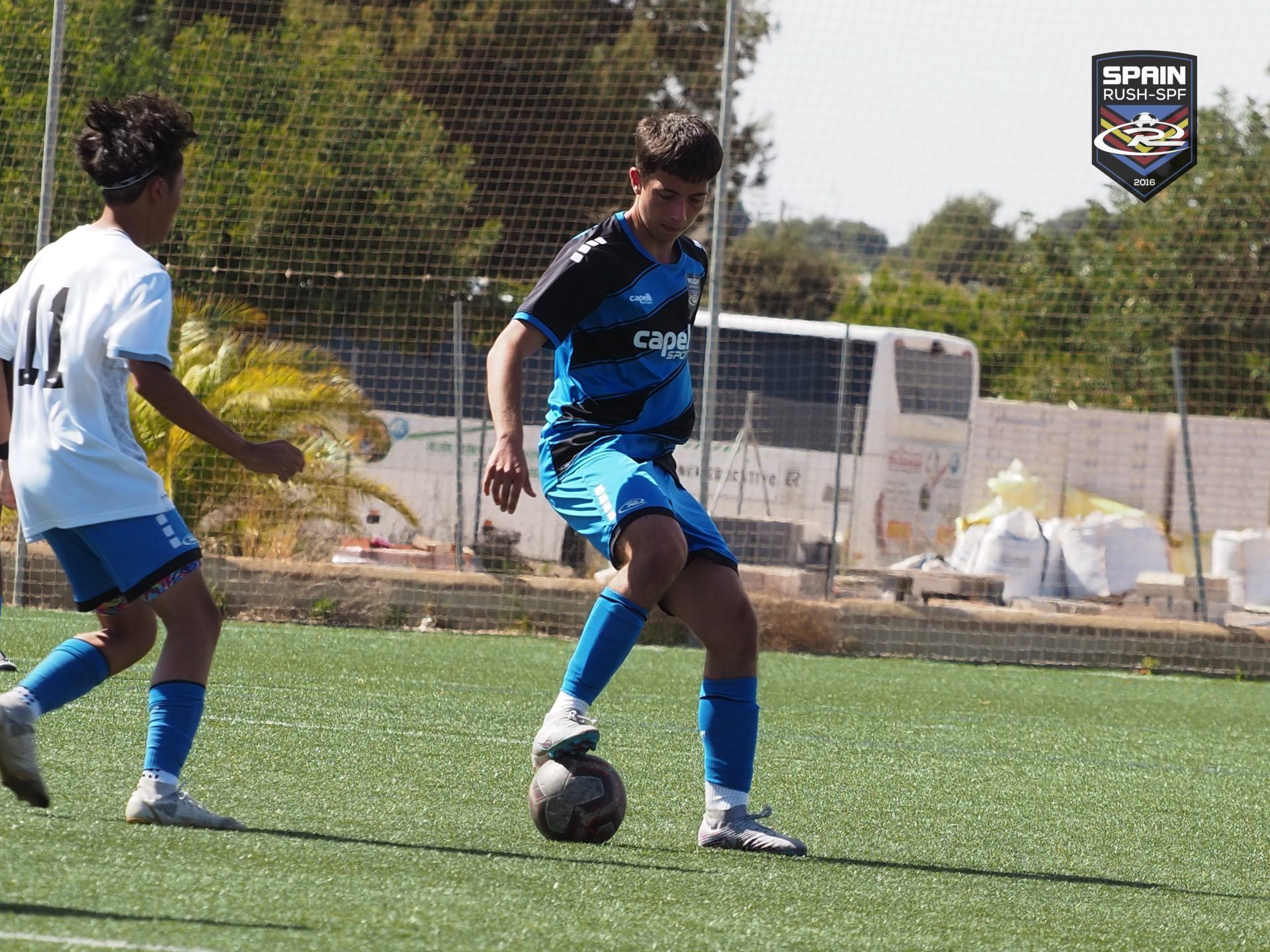 Two soccer players in blue uniforms contesting a ball on a field.