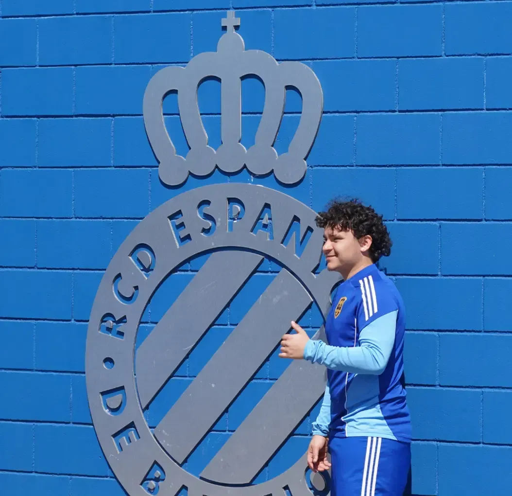 Person in blue sportswear posing by a blue RCD Espanyol logo on a brick wall