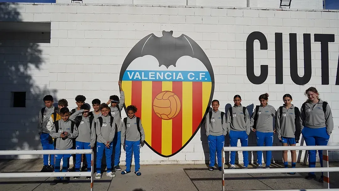 Group posing beside Valencia C.F. crest outside a building, with “CIUT…” sign in background