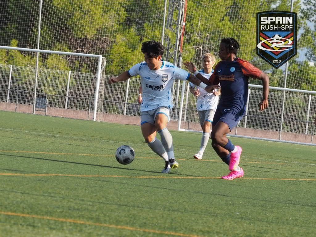Two soccer players sprint toward the ball on a grassy field near the goal