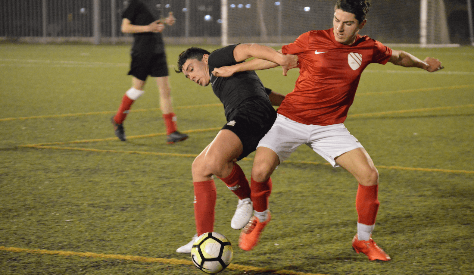 Two soccer players battling for the ball on a wet field at night