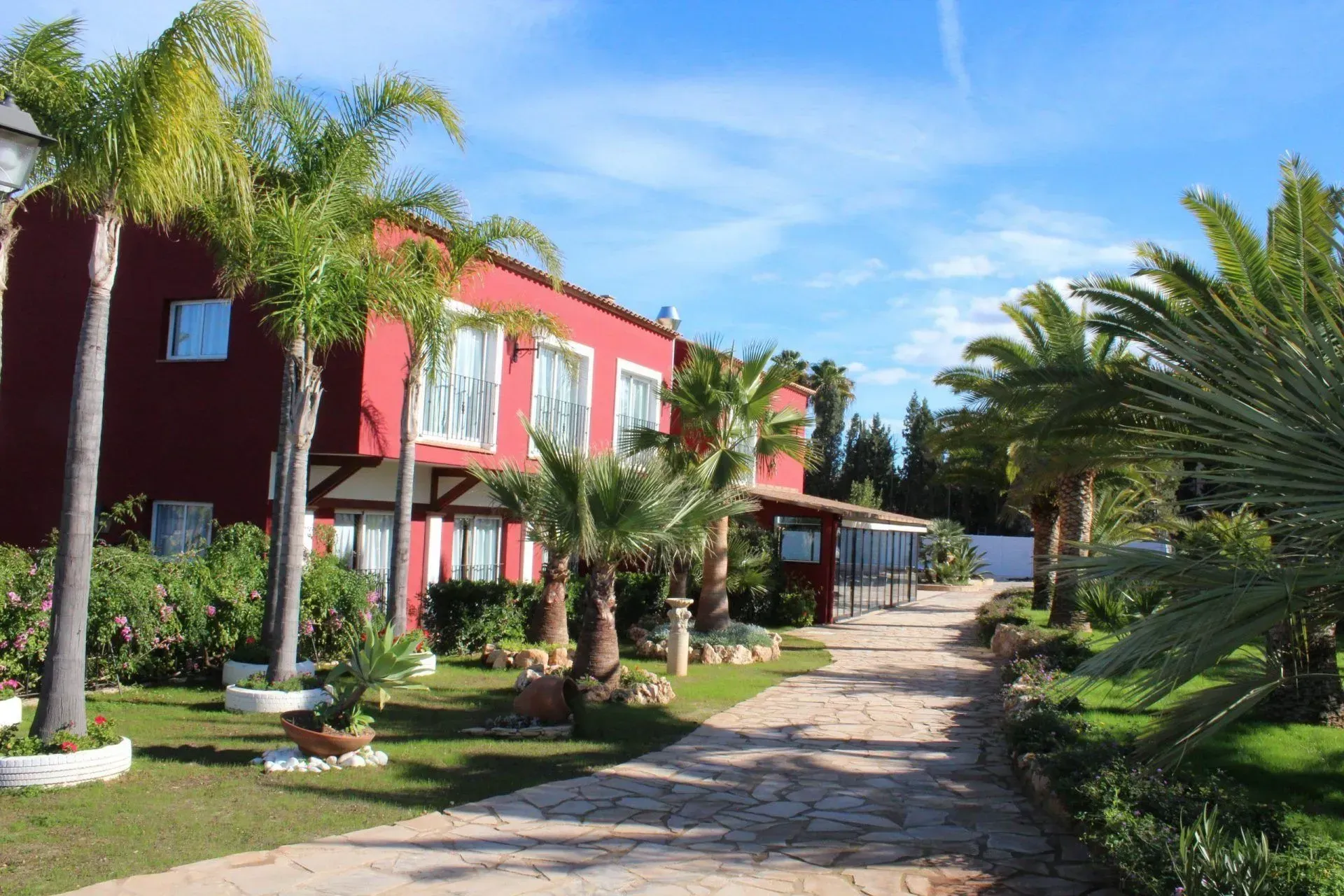 Palm-lined walkway beside a red building in a sunny tropical resort garden