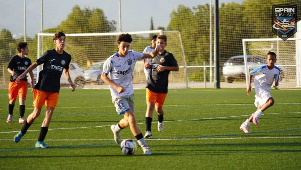 Soccer players chasing the ball on a sunny field, with one player dribbling toward goal