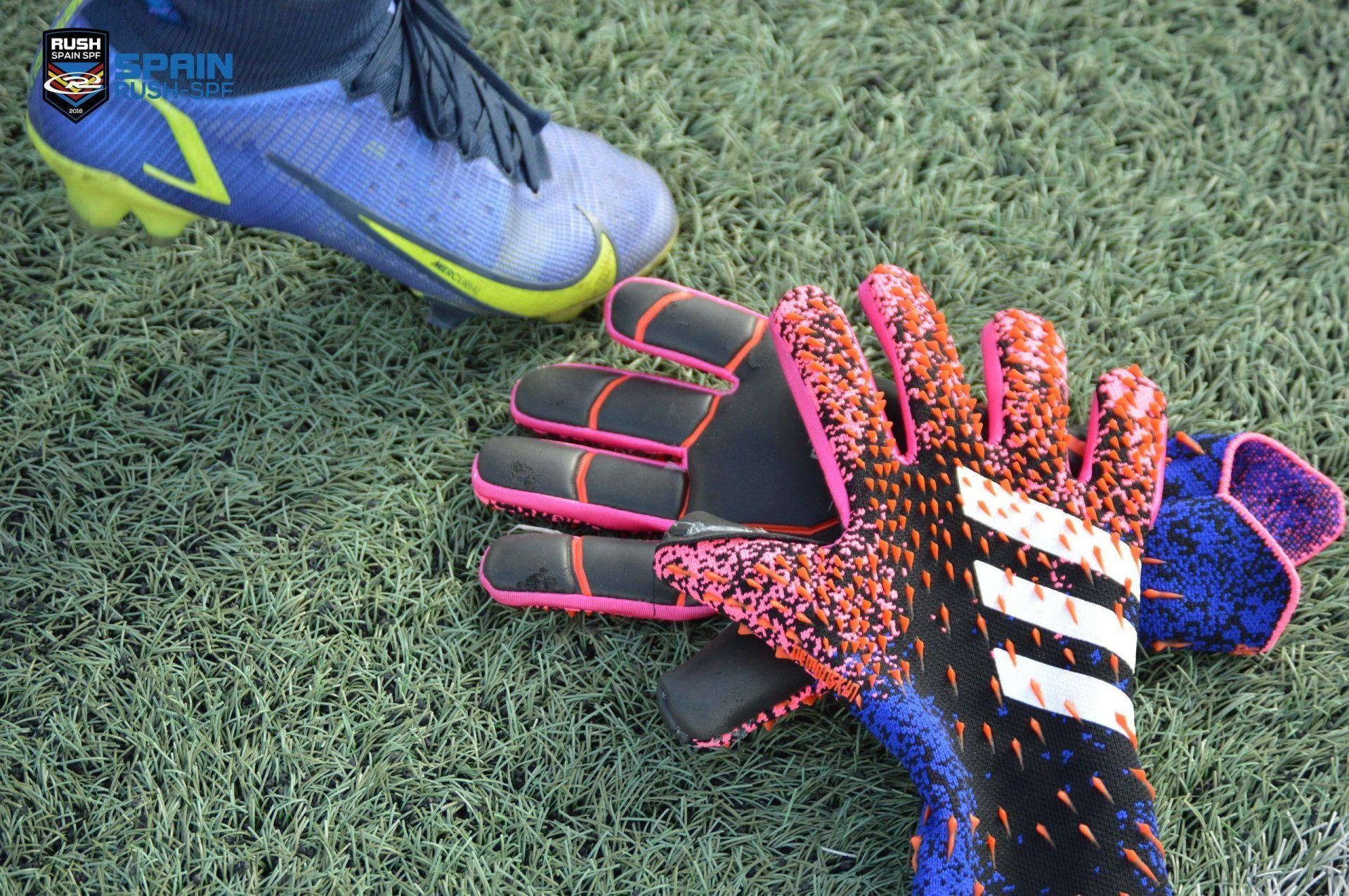 Blue soccer cleat and colorful goalie gloves on artificial turf