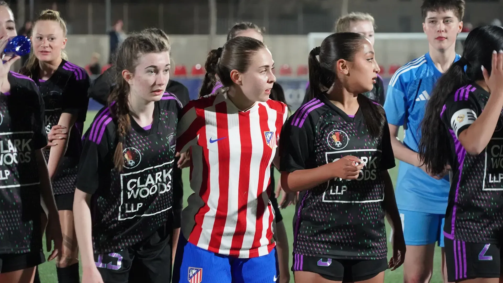 Youth soccer players in black and red-striped jerseys stand together on the field during a match