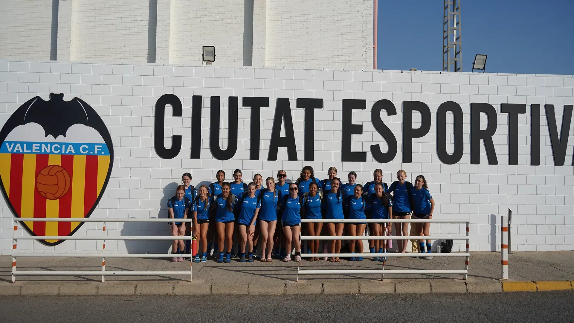 Valencia CF youth team posing in blue kits in front of Ciutat Esportiva sign