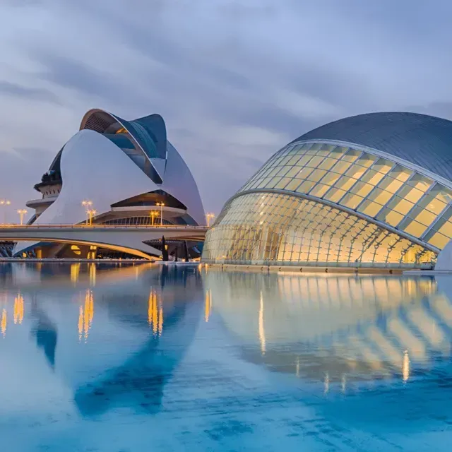 Modern waterfront buildings with curved glass domes reflected in calm blue water at dusk