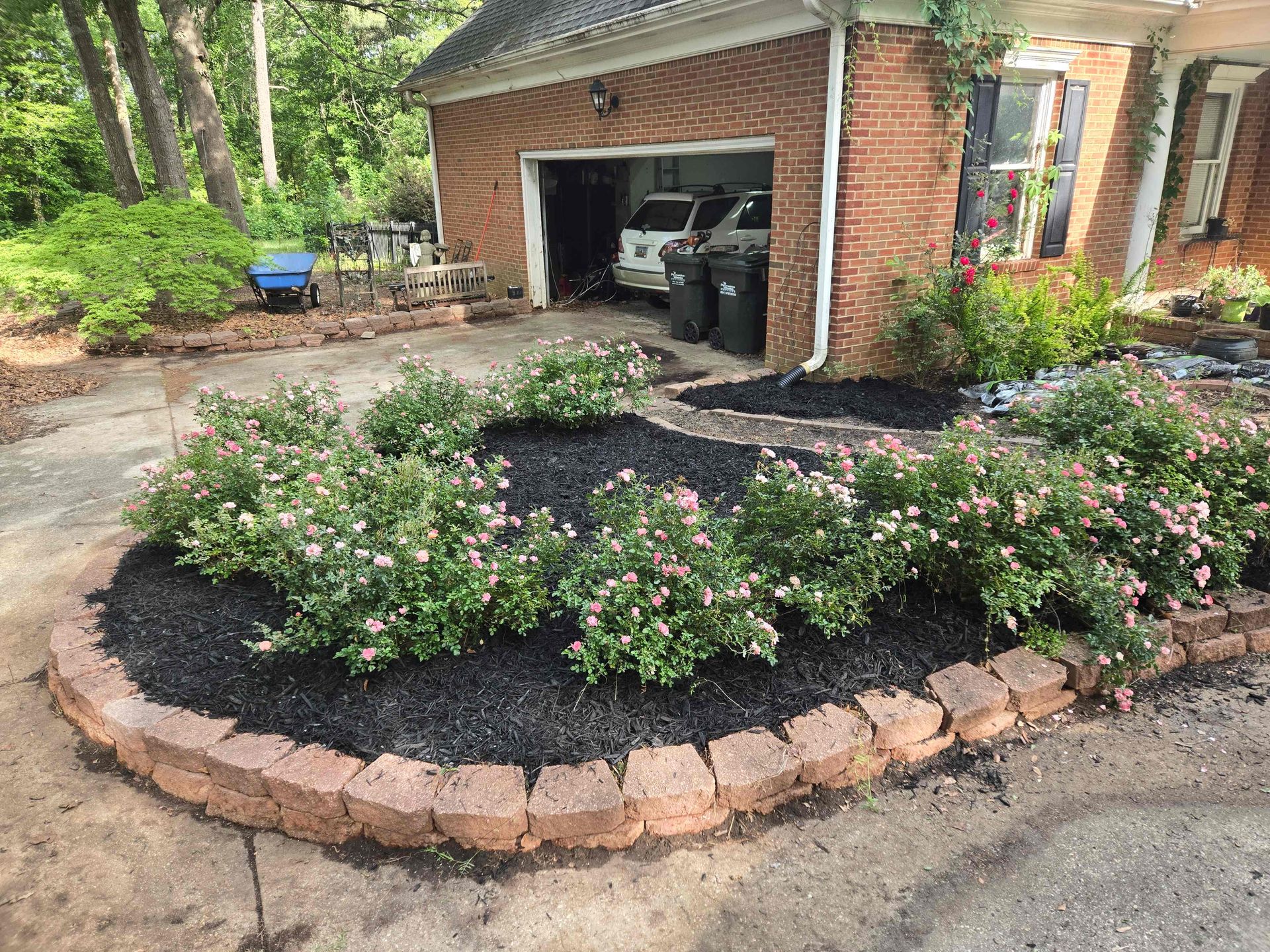 Brick house with open garage and landscaped flower bed bordered by stone pavers