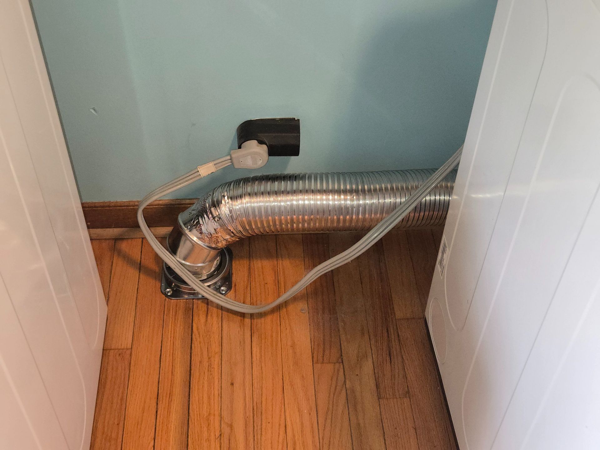 Flexible silver duct and hoses on a wooden floor in a white utility closet