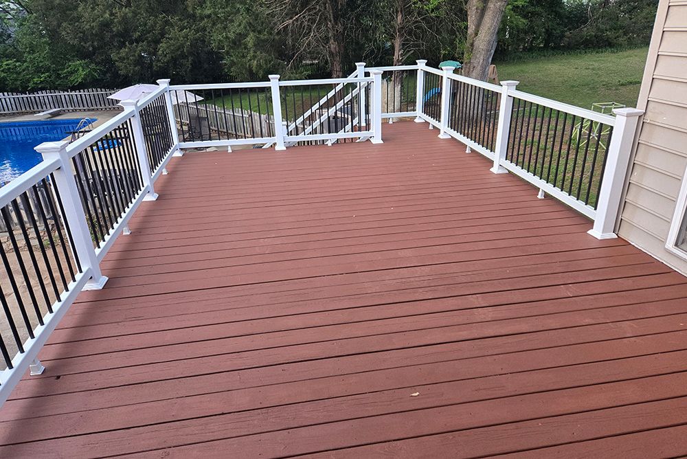 Brown composite deck with black railings, white posts, and a view of a pool and yard.