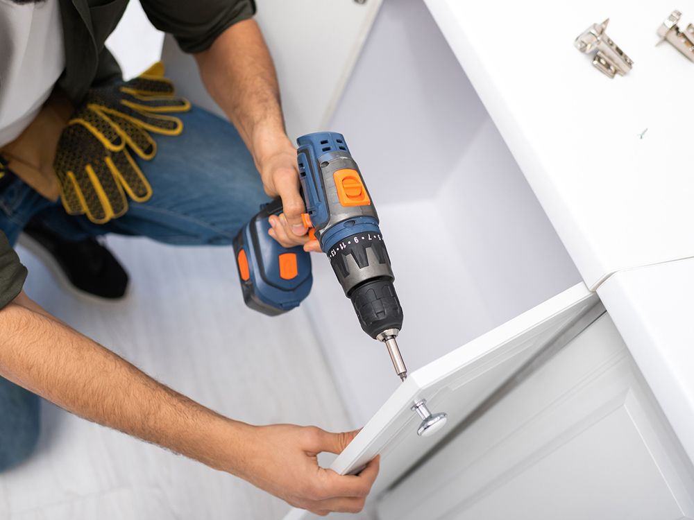 Man using a drill to attach a cabinet door; indoor setting, blue and white.