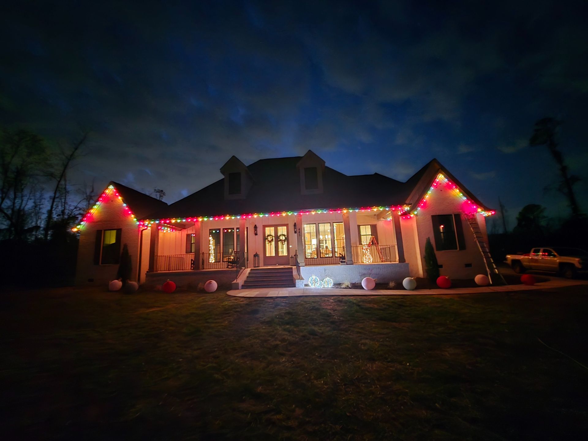 A home at twilight decorated with vibrant, multi-colored Christmas lights along the roofline and porch.