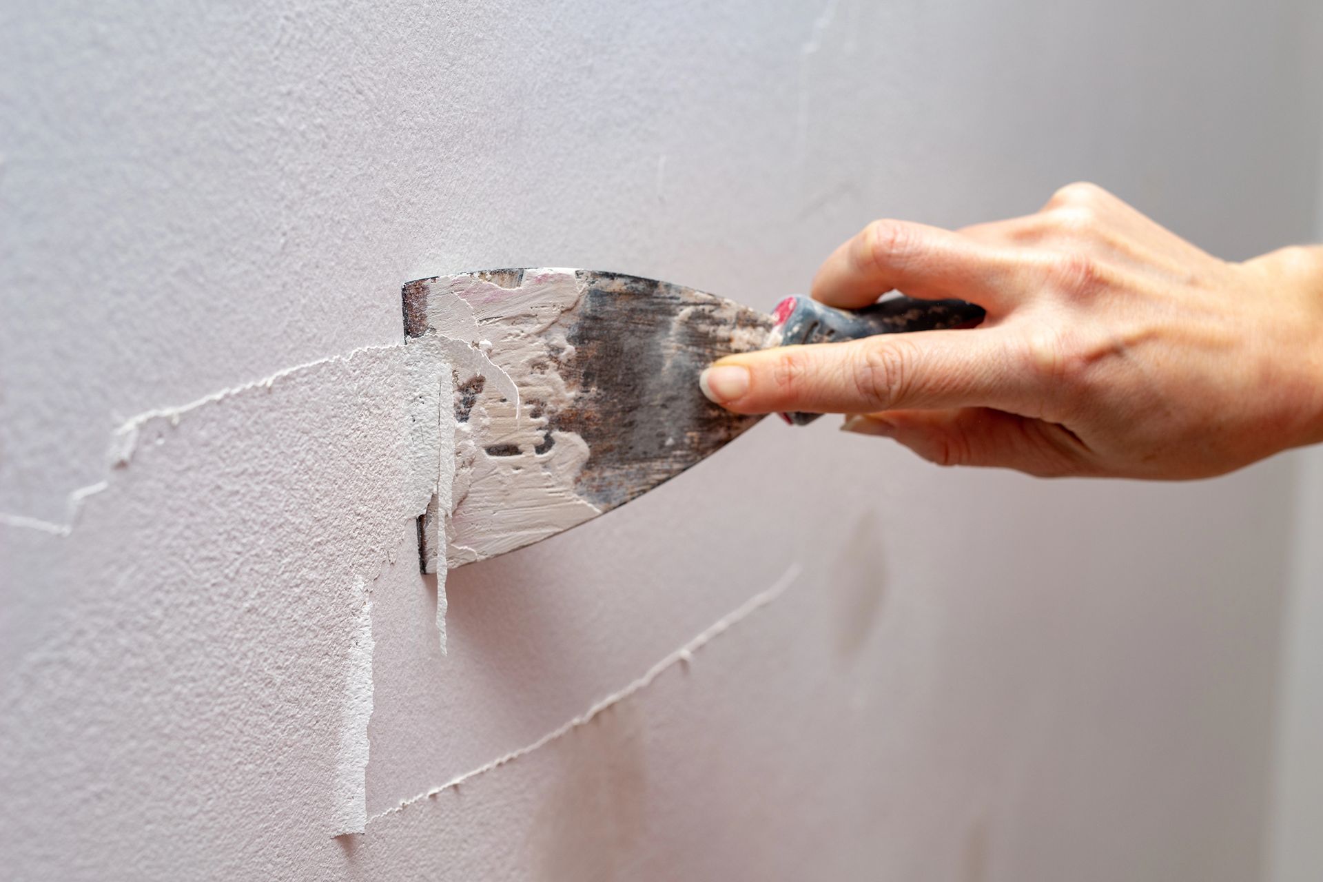 Hand using a putty knife to apply spackle to a wall, smoothing the surface.
