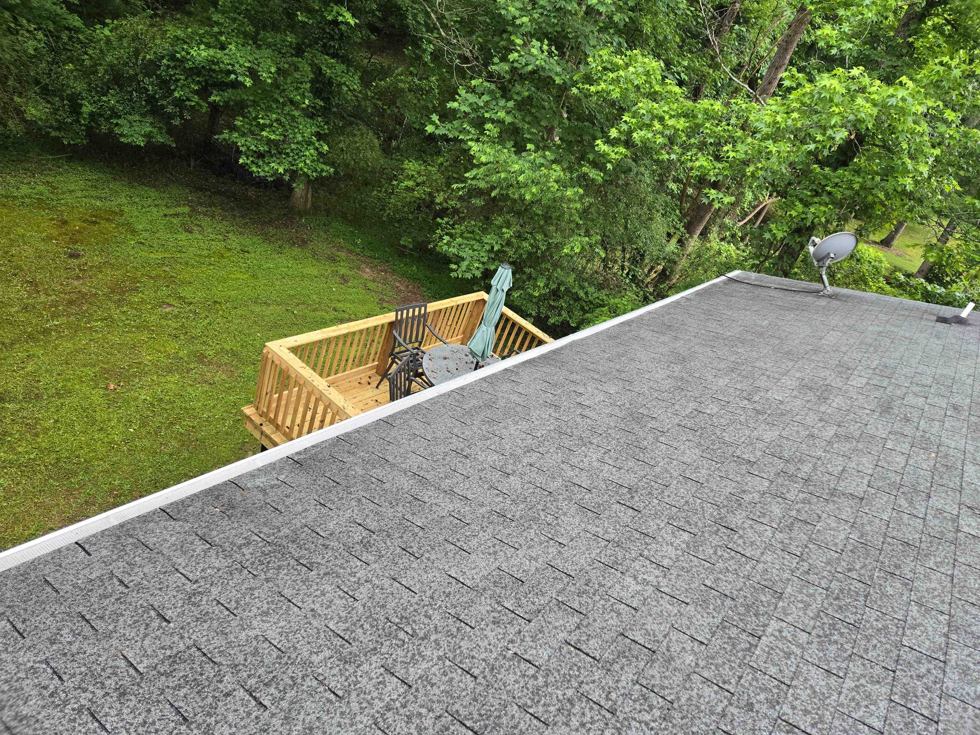 Gloved hand reaching into a gutter full of leaves, near a shingled roof edge.