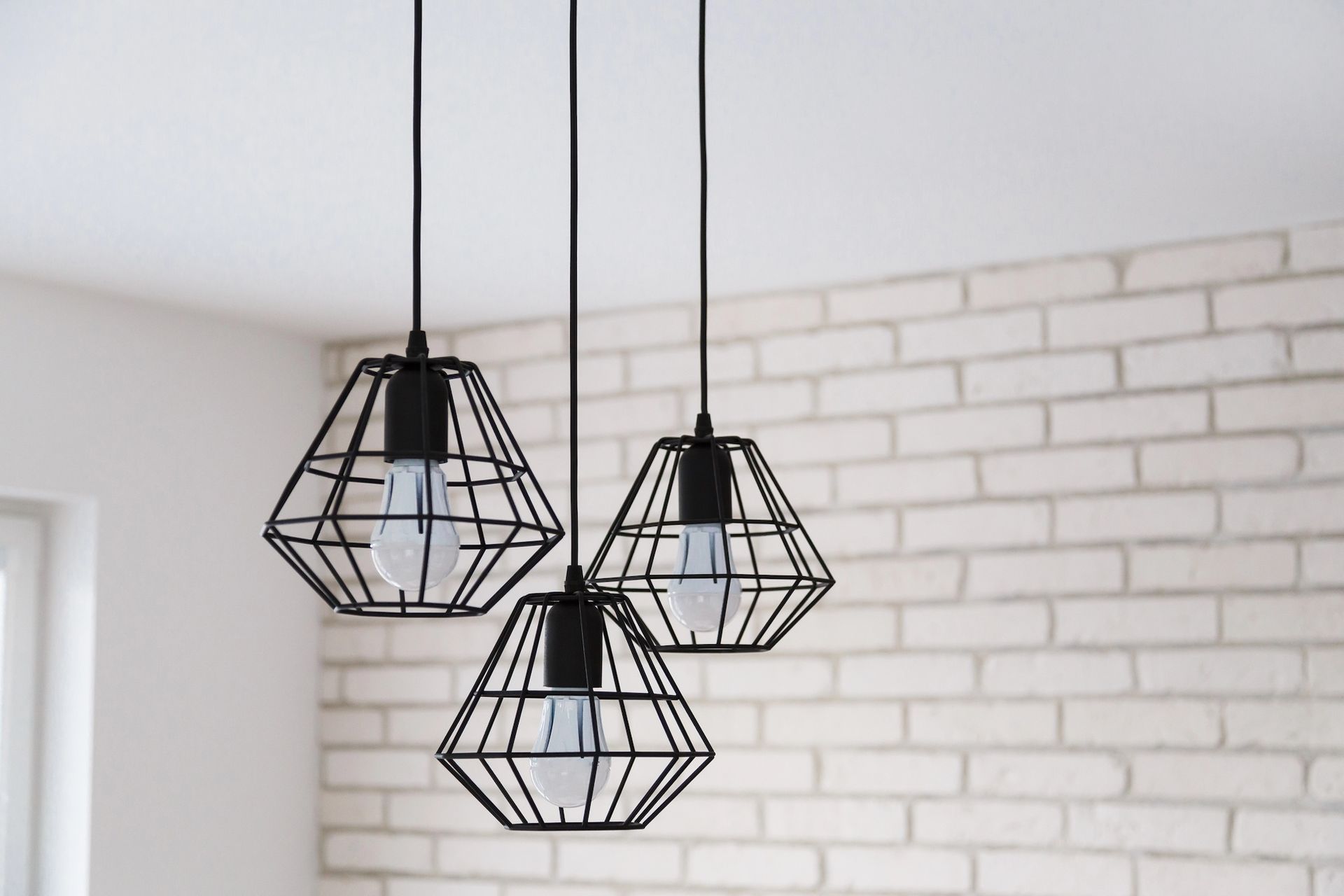 Three black geometric pendant lights hanging in front of a white brick wall