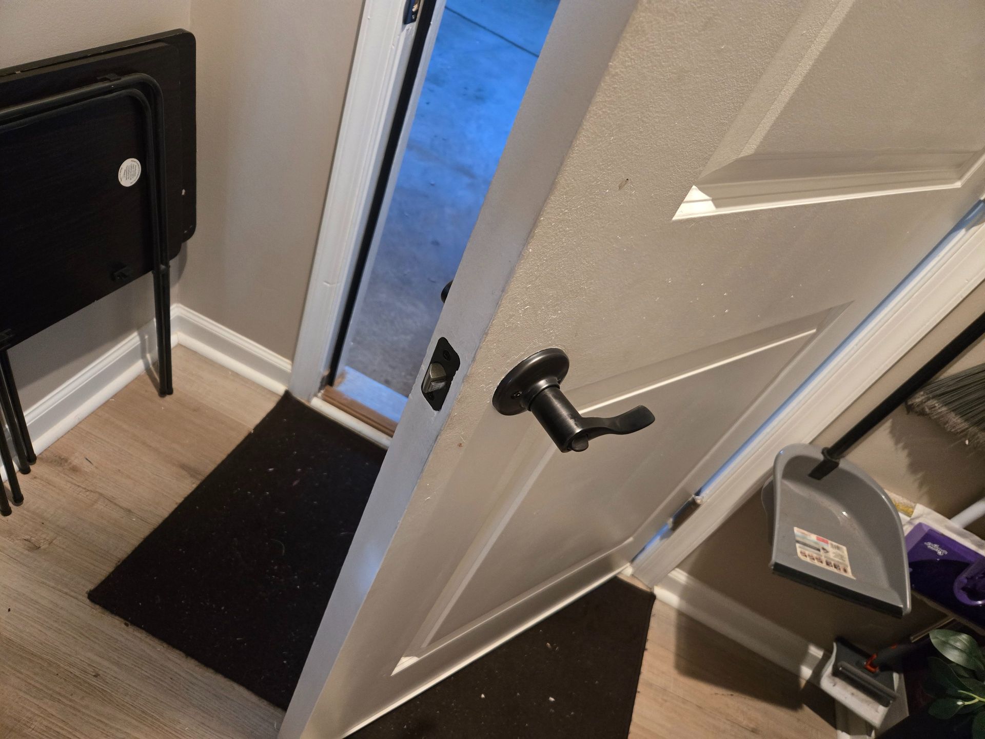 Open door with a black handle beside a narrow hallway, showing a blue-lit room beyond.