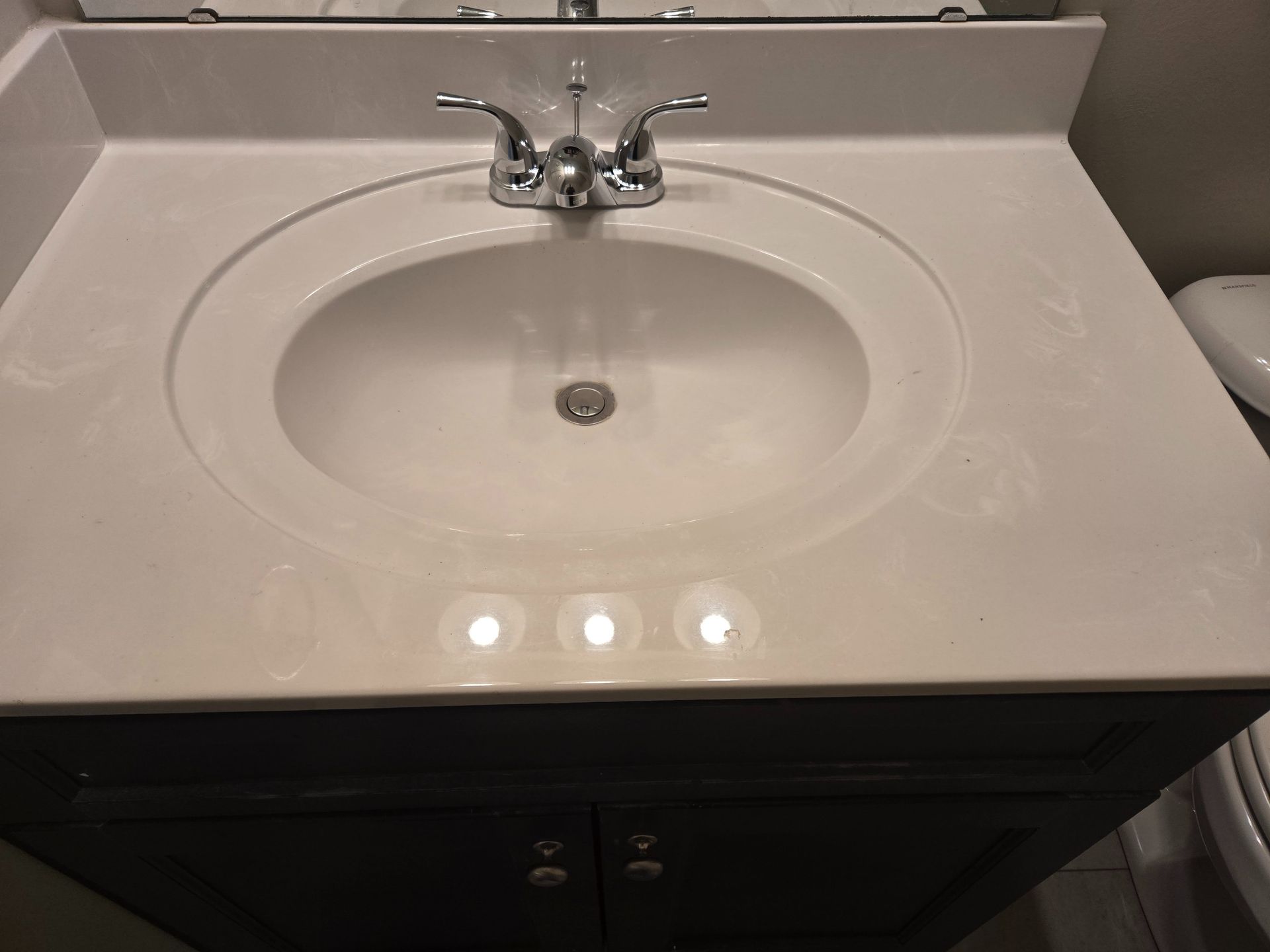 White bathroom sink with chrome faucet in a dark vanity countertop.