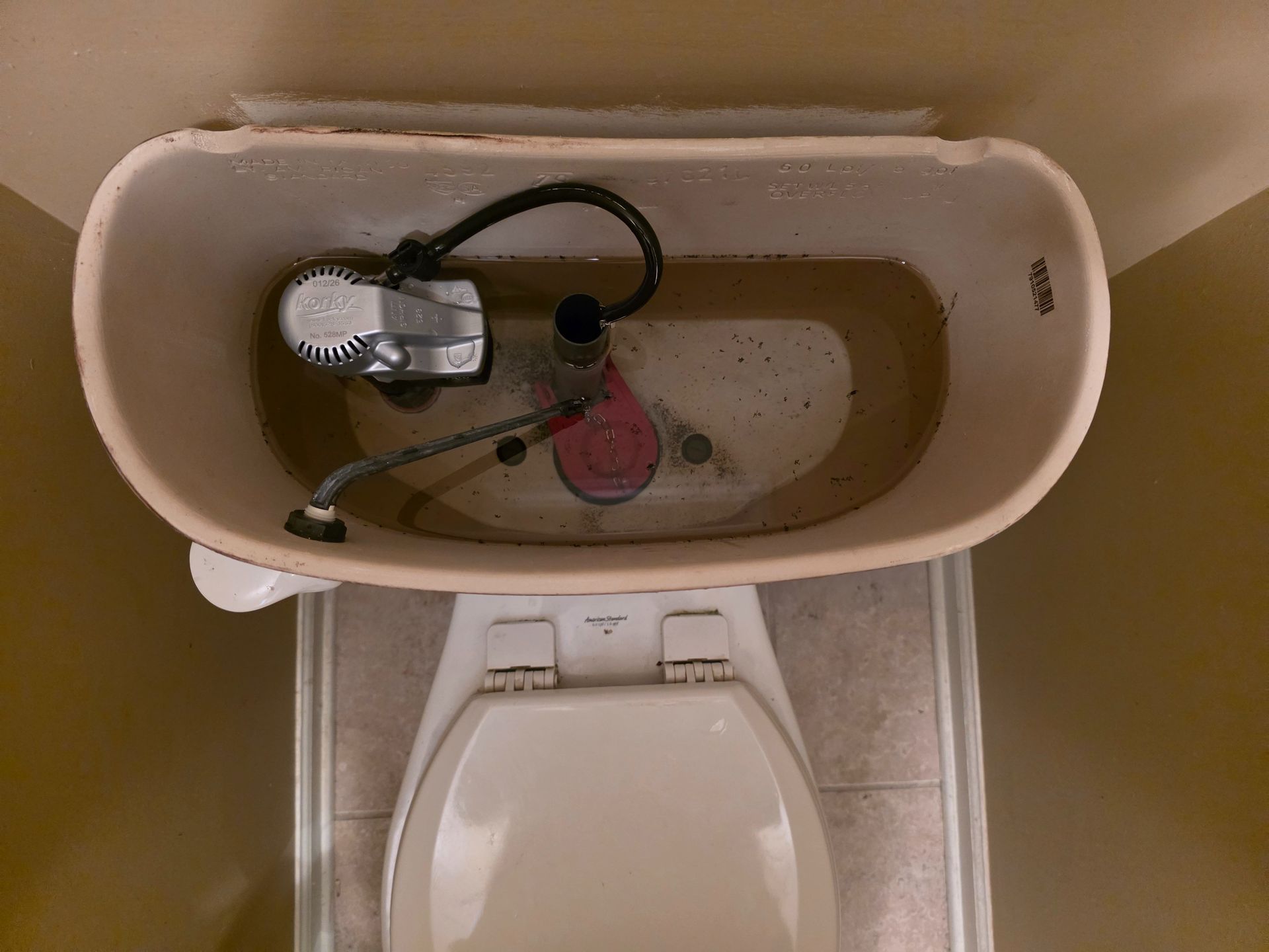 Top-view of a toilet tank with exposed plumbing and a pink cleaning ball above the bowl.