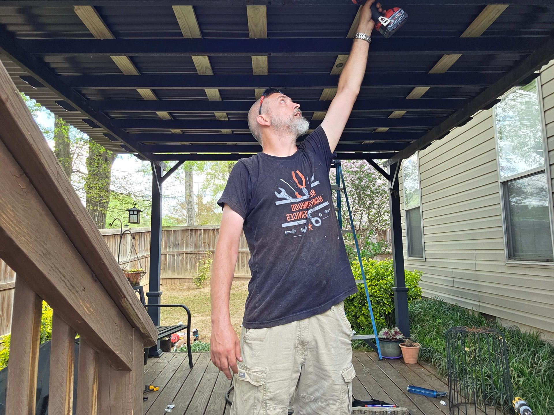 Man standing under a deck, reaching up to inspect or repair the ceiling.