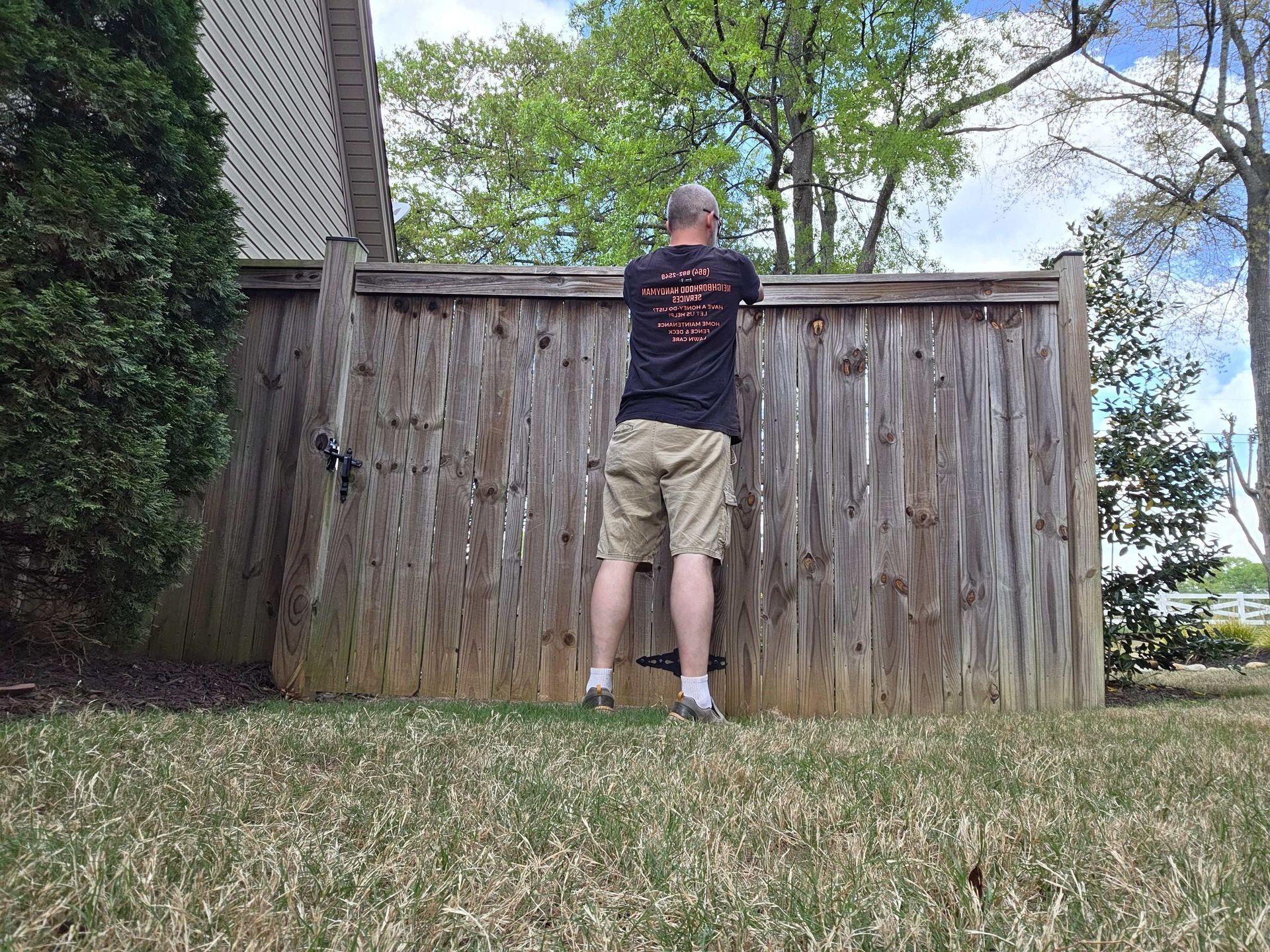 Person standing on a wooden fence in a backyard, facing a weathered shed wall.