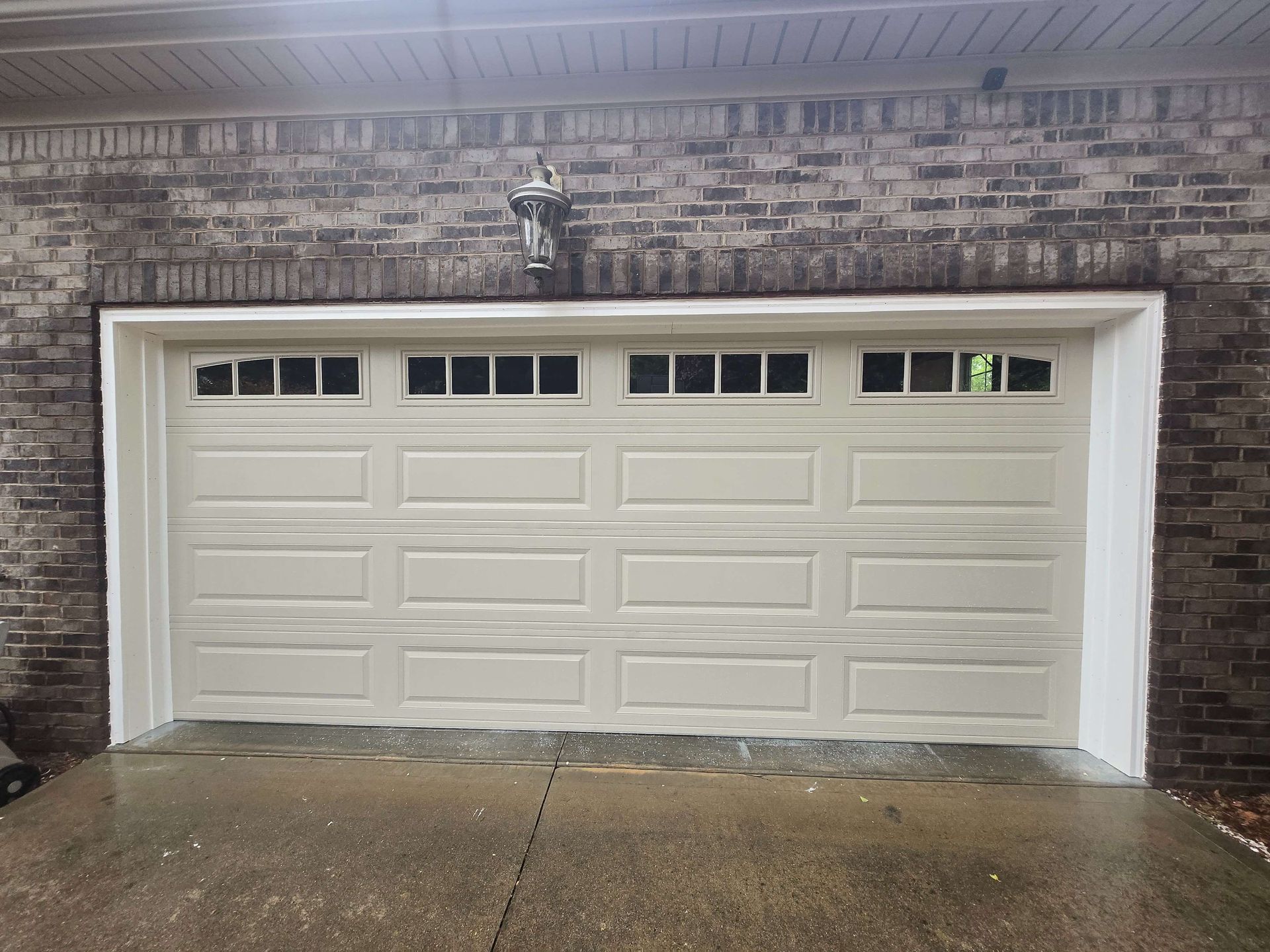 White double garage door on a brick house with wet driveway and small lights above.