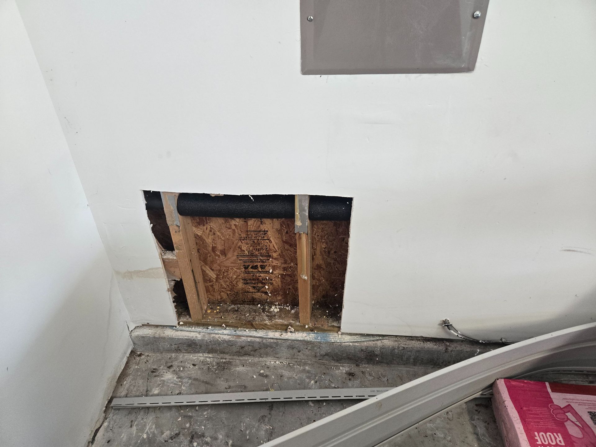 Damaged drywall with exposed wood framing near a corner, and a gray panel leaning in front.