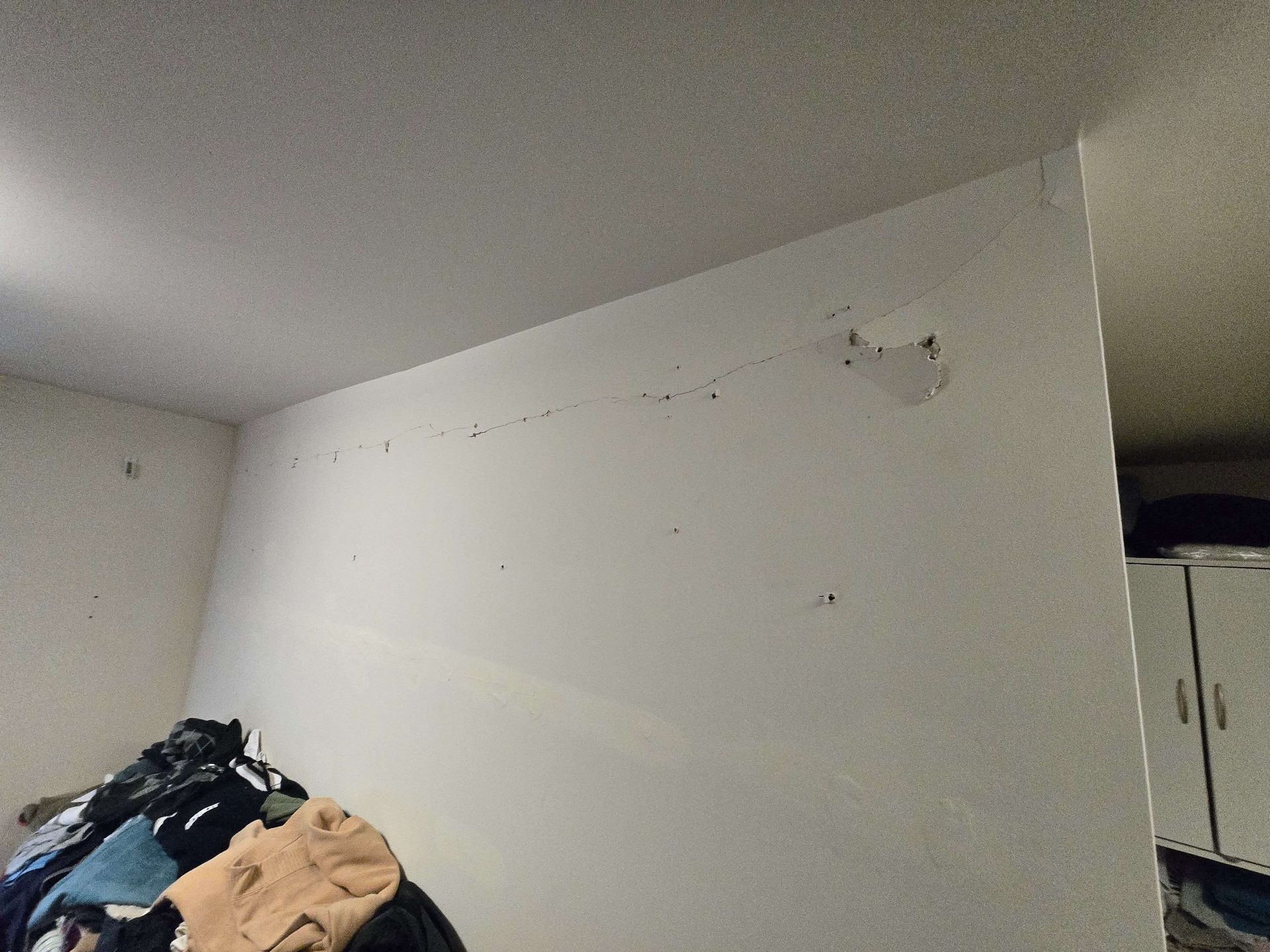 White interior wall with a small damaged patch, next to a closet and piled clothes in a room