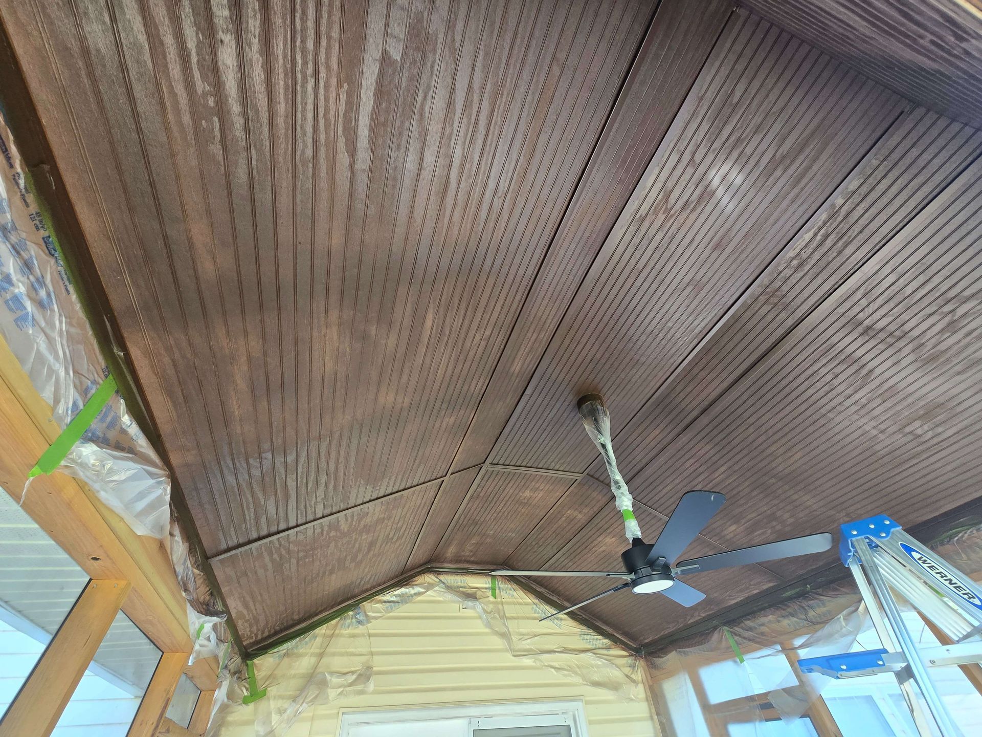 Damaged brown porch ceiling with sagging panels, exposed wooden beam, and a ceiling fan below