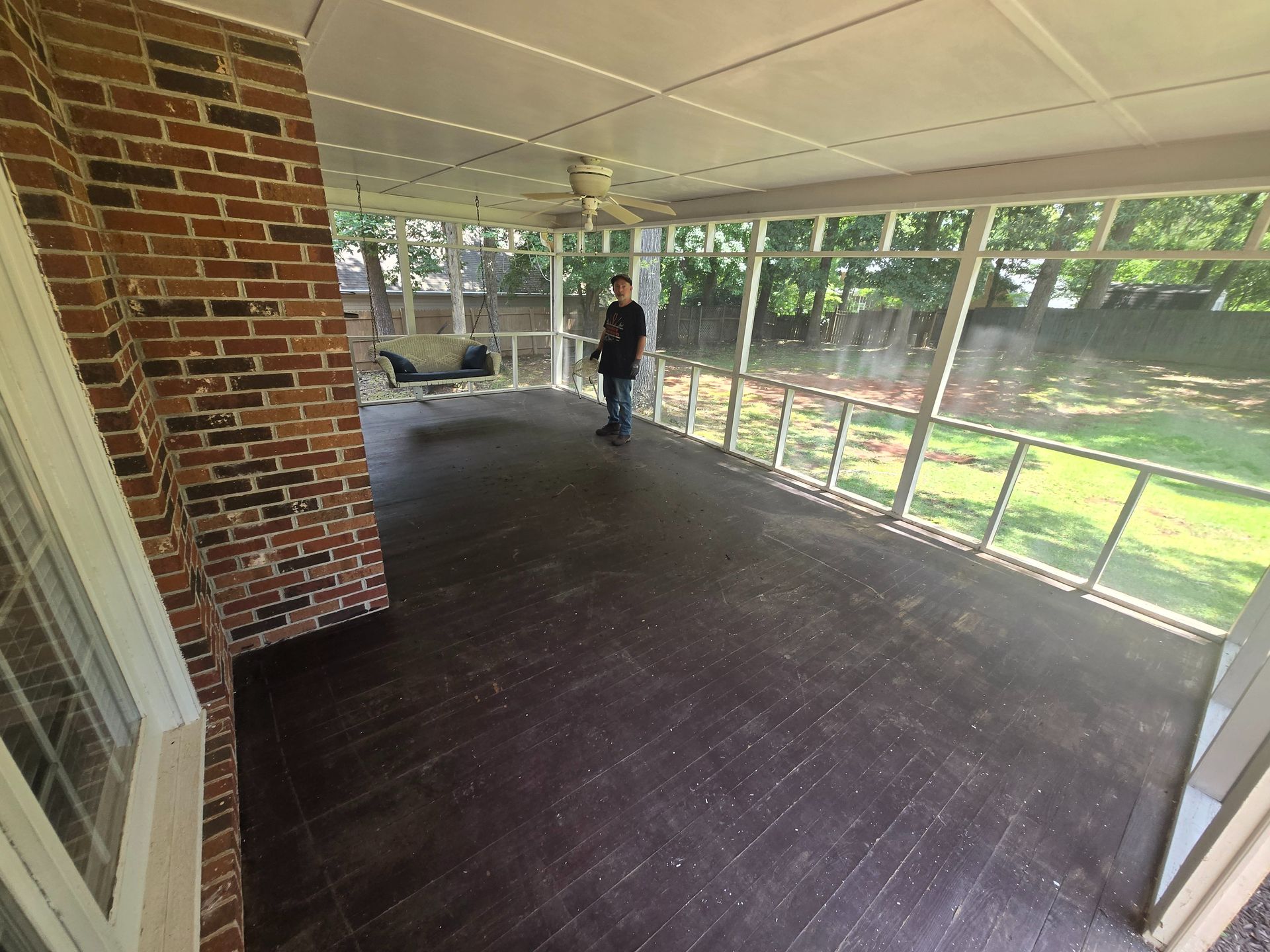 Screened porch with dark wood floor, brick wall, and a person standing near the windows.