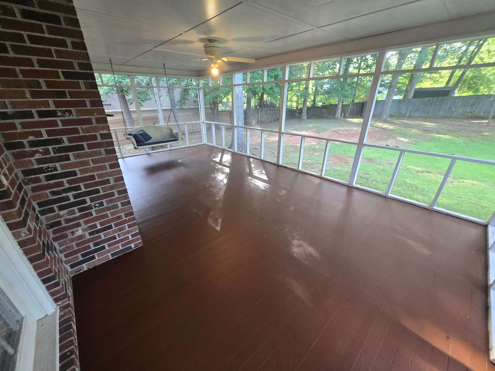 Screened porch with glossy brown floor, brick wall, and view of green backyard.