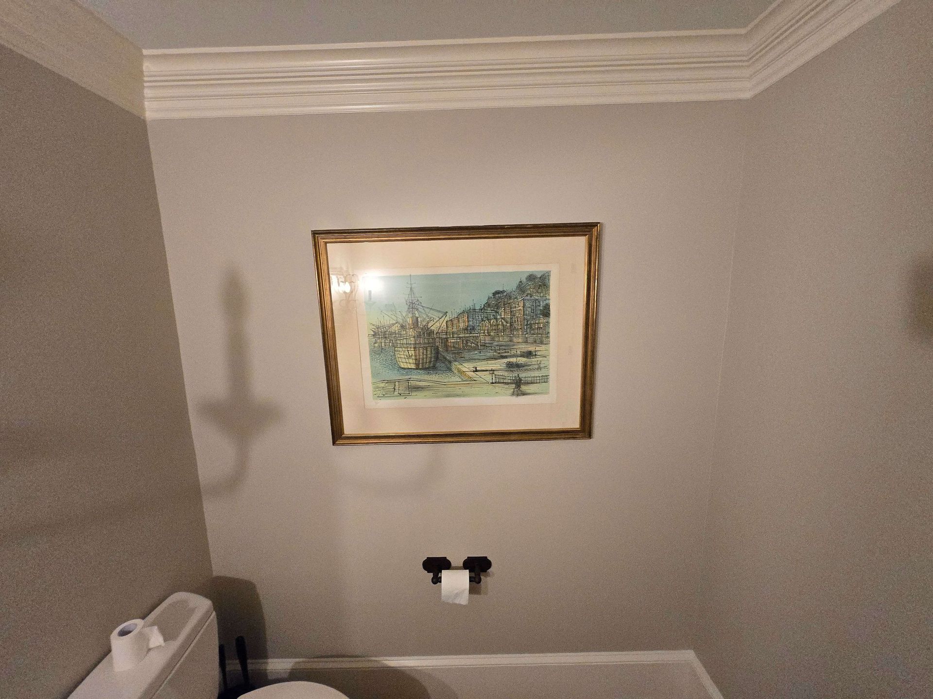Framed landscape print on a light gray wall above two black wall fixtures, with white crown molding.