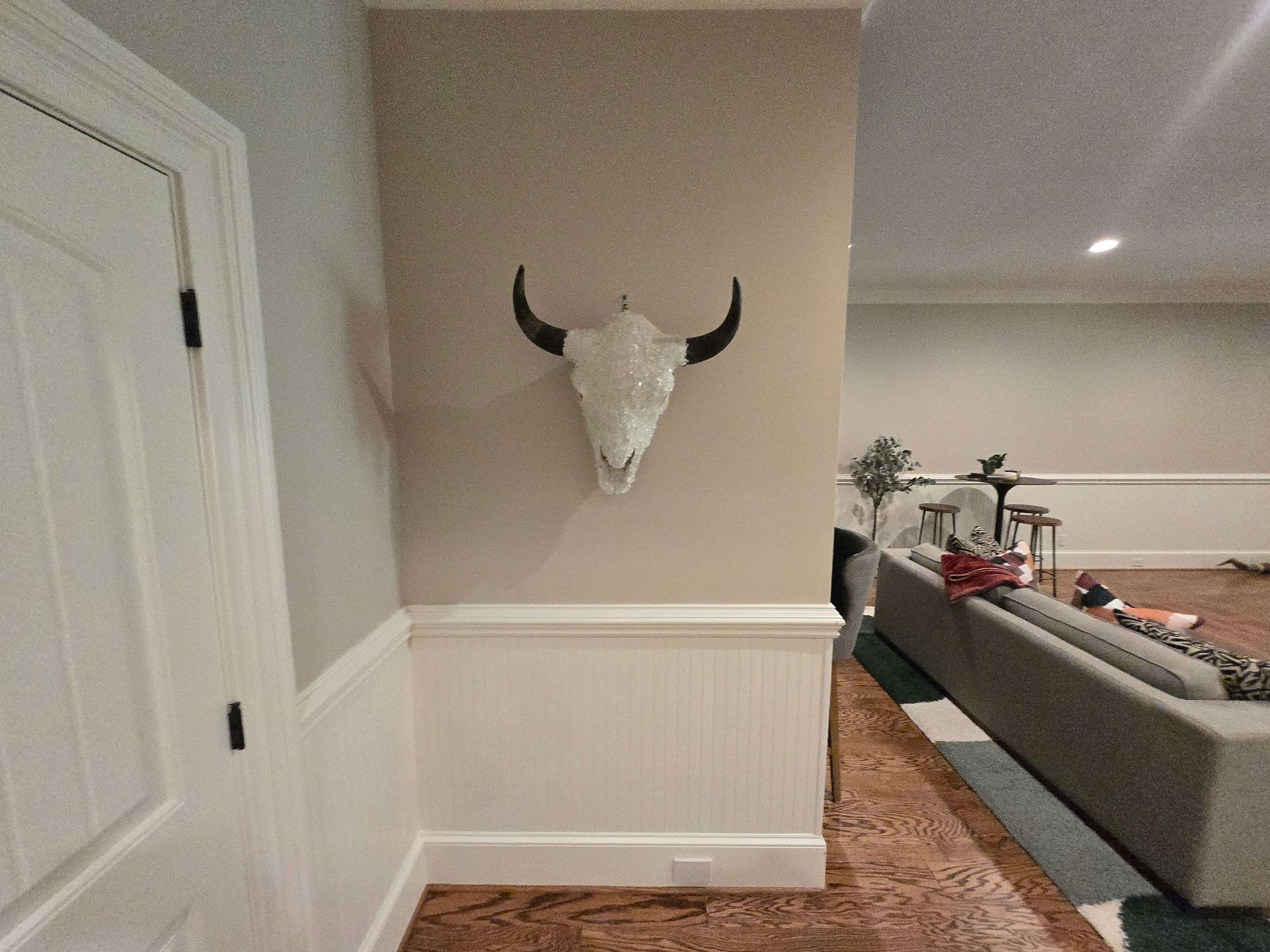 Hallway with a mounted white bull skull on a beige wall beside a carpeted living room.